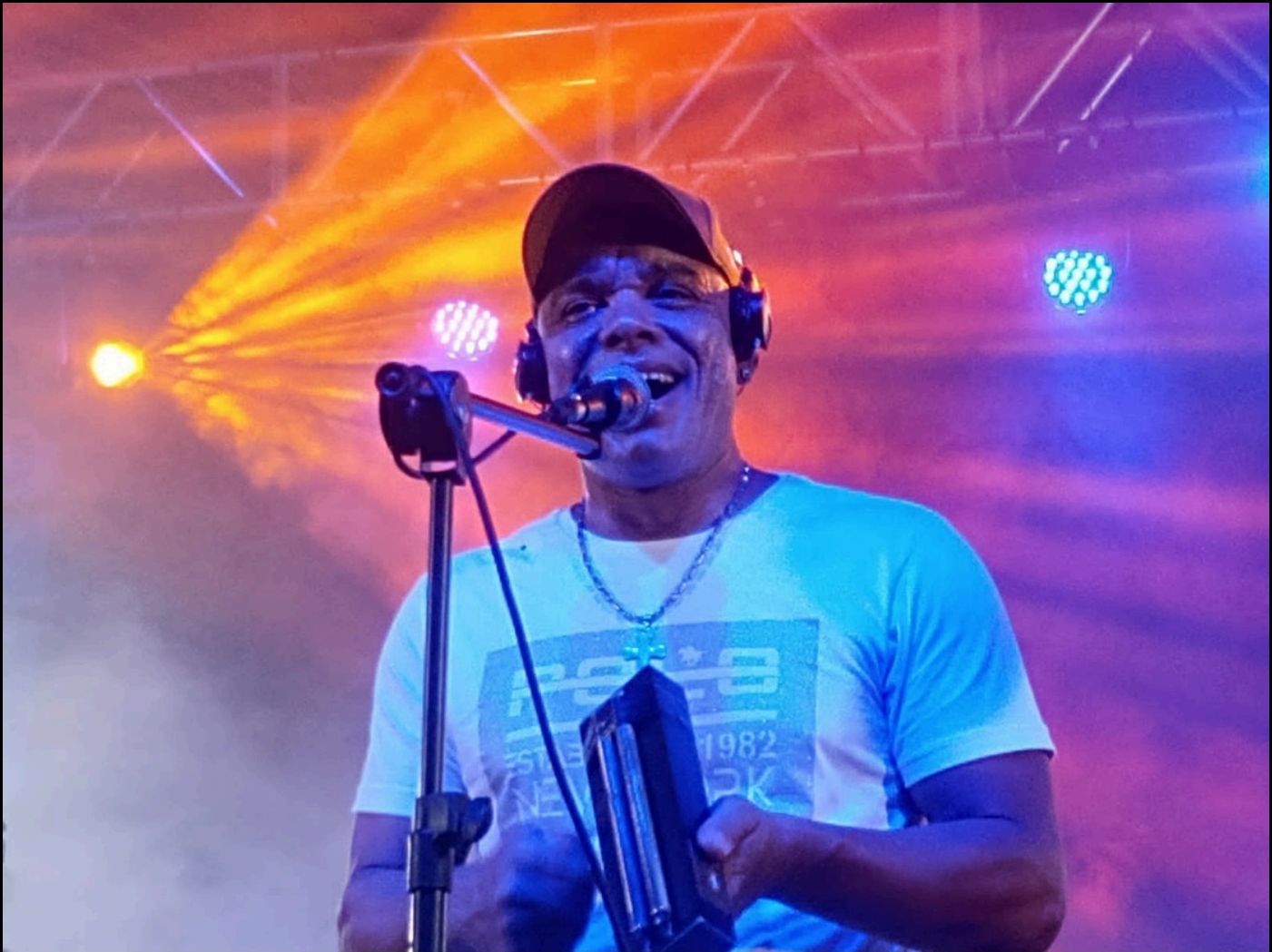 Alexandre Cruz no palco, sob luzes vermelhas e violeta, segurando o microfone